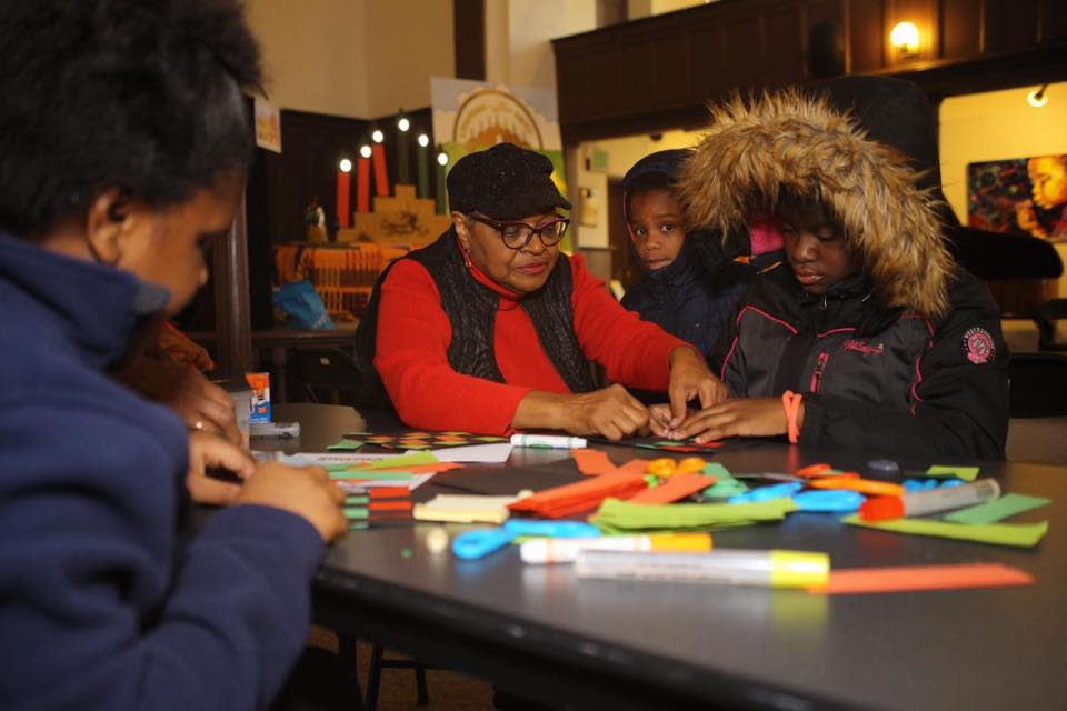 Woman and children doing crafts in front of Kwanzaa display